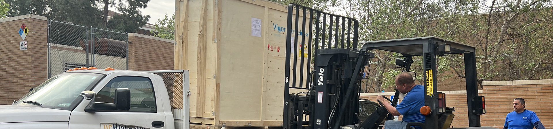 A Receiving Services worker uses a forklift to load a crate onto a flatbed truck.